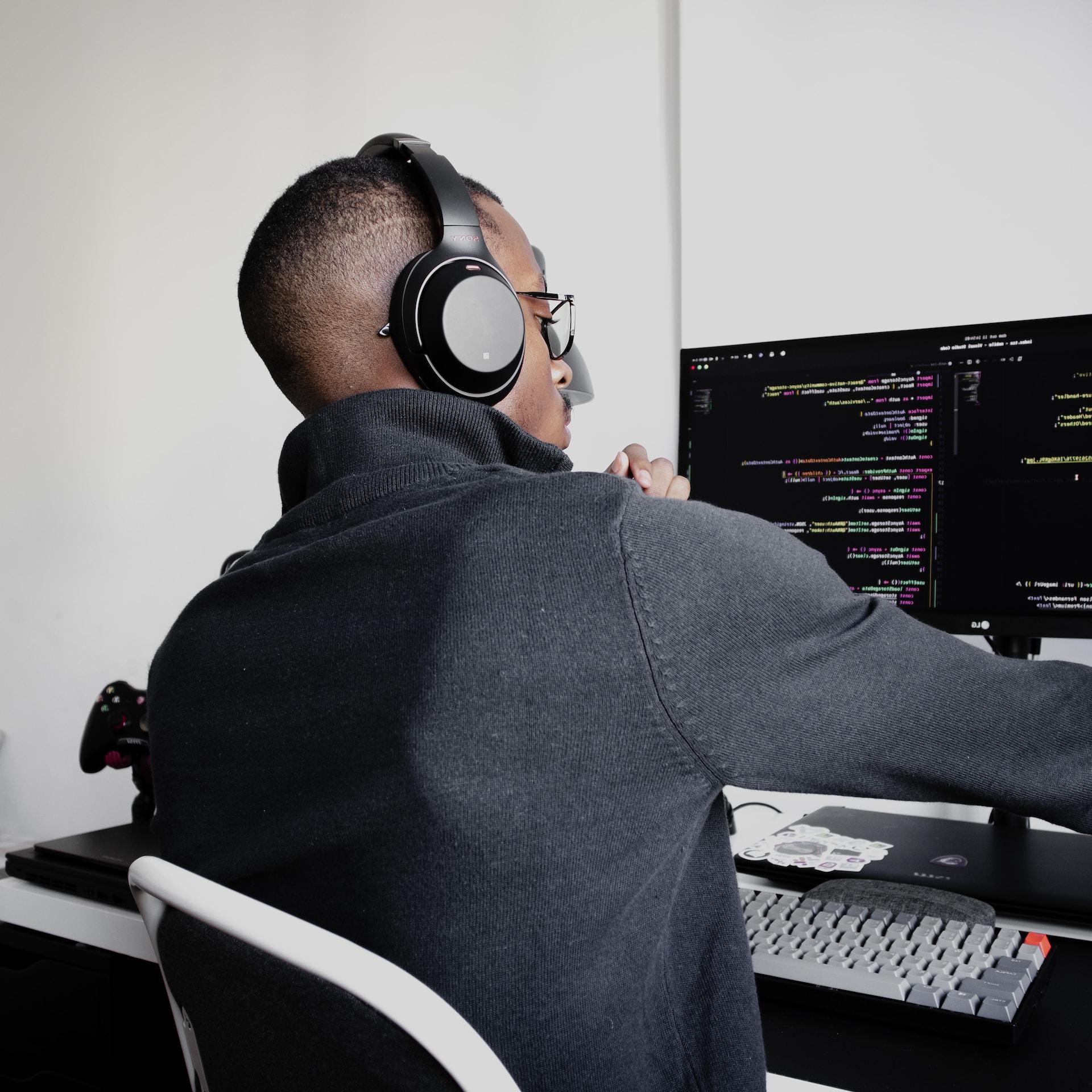 A black man with headphones sitting in front of a computer