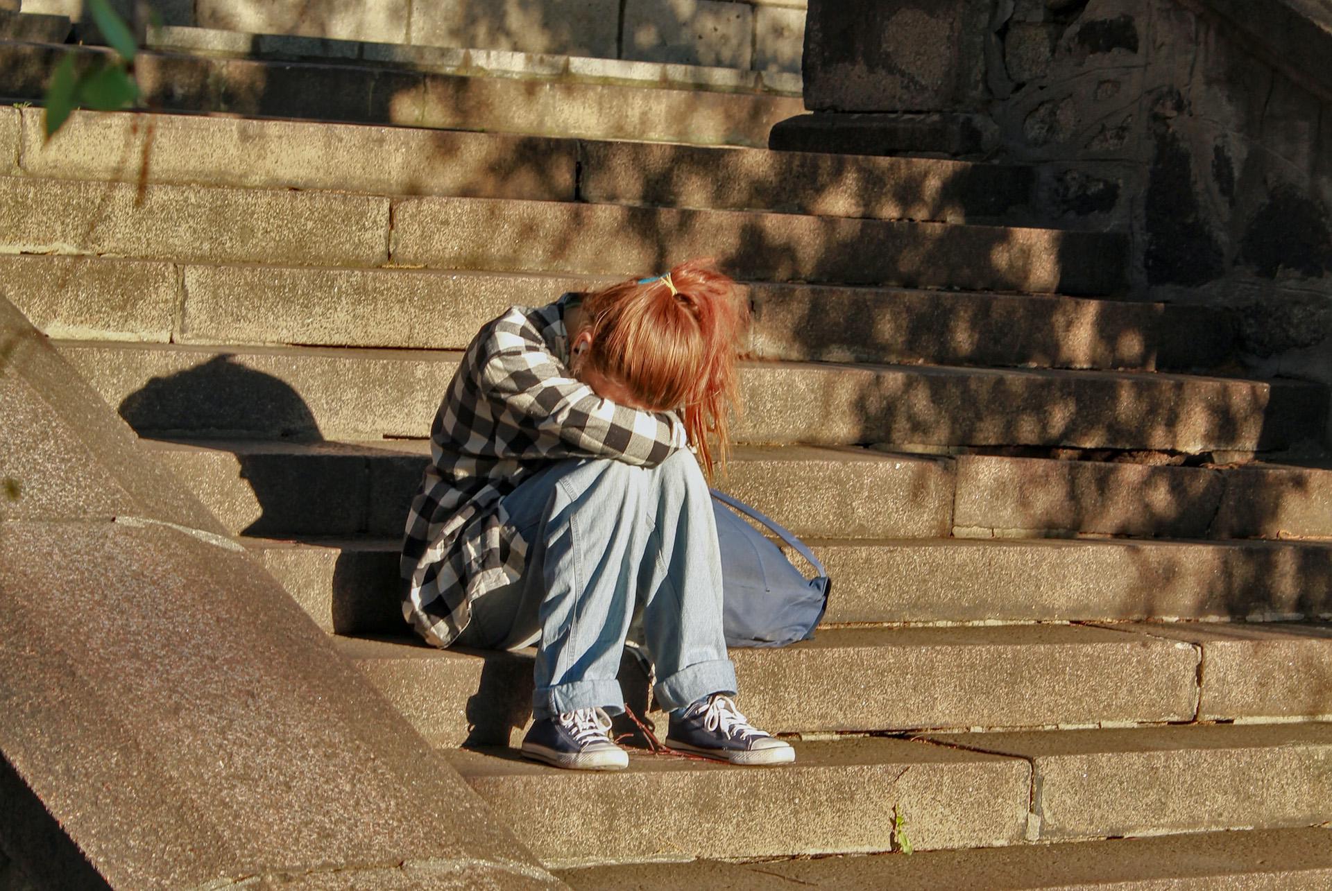 woman in black and white checkered top sitting on concrete stairs with her head down